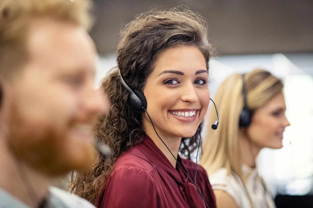 A smiling woman wearing wearing a headset sitting between two other workers with headsets