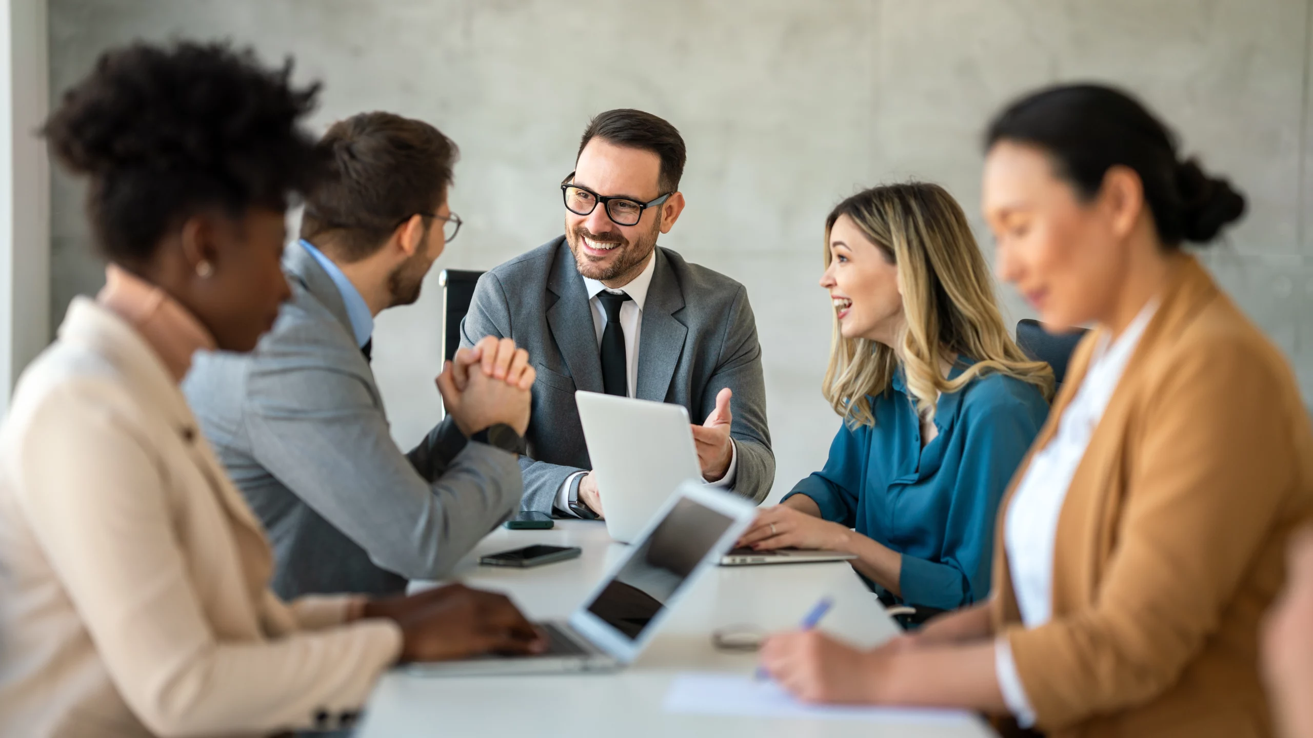 A multicultural group of people dressed in business clothes have a discussion around a long table